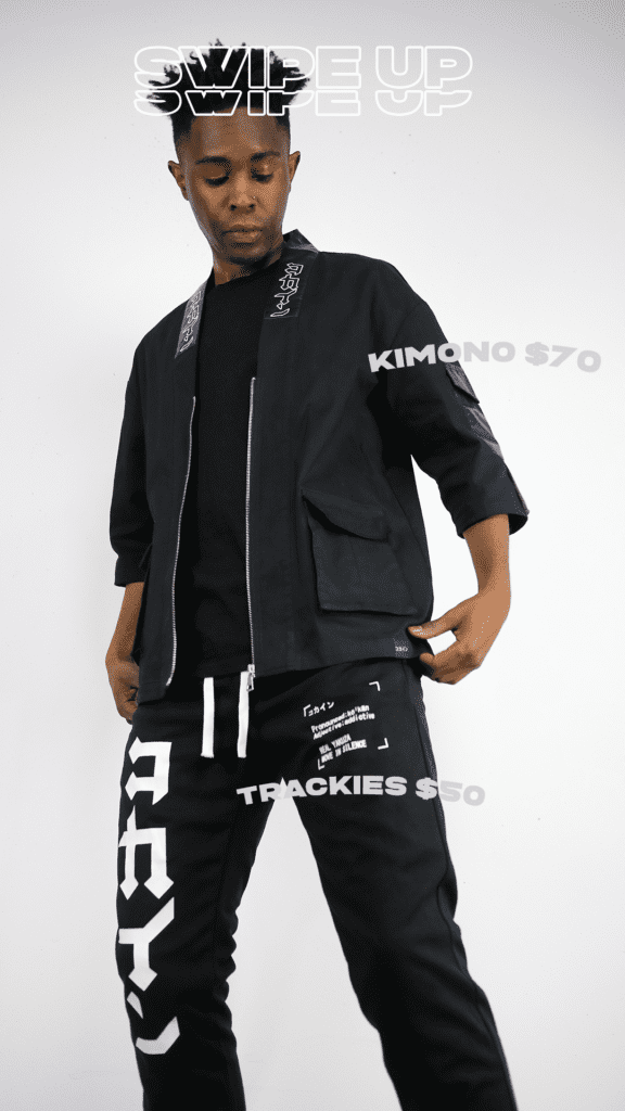 Dark skinned male wearing tech wear kokaine kimono and track pants, that have heavily branded text on them.