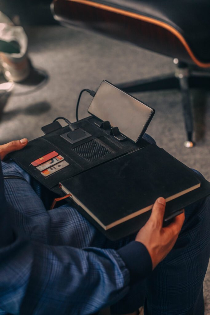 NOTA suit shop tailor, man in custom suit sitting on the chair, in suit shop setting, custom tailor, houndstooth tailors, open with phone charging and credit cards in notebook