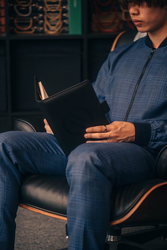 NOTA suit shop tailor, man in custom suit sitting on the chair, in suit shop setting, custom tailor, houndstooth tailors, holding notebook