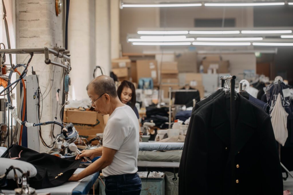 Man cutting leather and stitching zips using sewing machine, man in workshop - nota