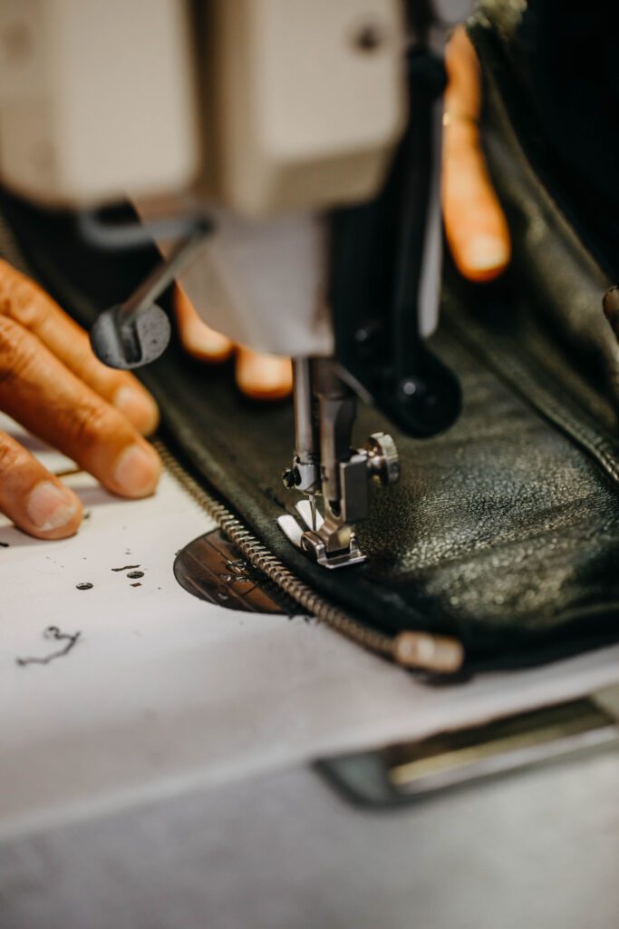 Man cutting leather and stitching zips using sewing machine - nota